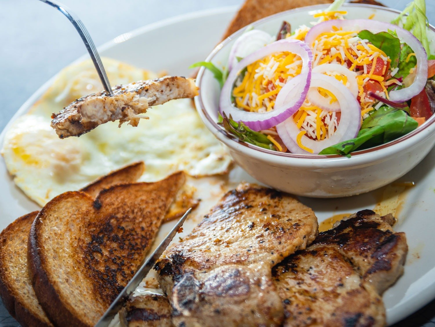 Grilled seasoned Pork Chops with two eggs, seasoned potatoes, and toast at Tasty Munch