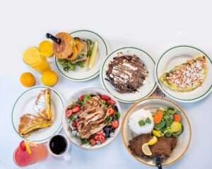Assorted breakfast and brunch plates including pancakes, fresh salad, burger, stuffed French toast, and Good Morning omelet at Tasty Munch Houston.